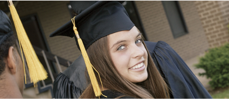 A new graduate in full graduation attire is looking over her shoulder and smiling