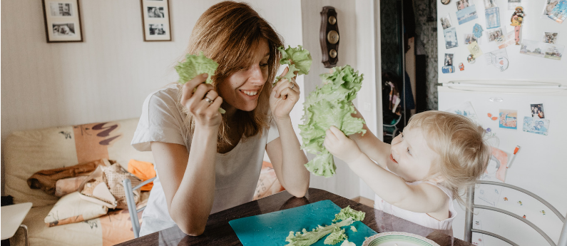 A mom and her toddler are playing with lettuce and smiling