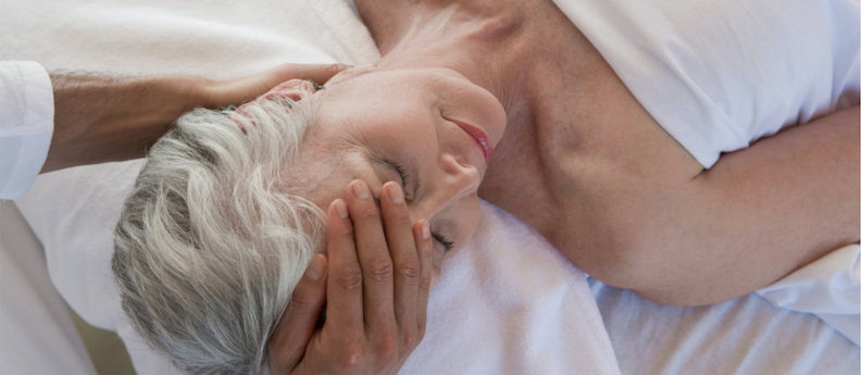 An older woman with white hair having her head massaged. Learn different massage techniques, including Oncology, at AMBI.