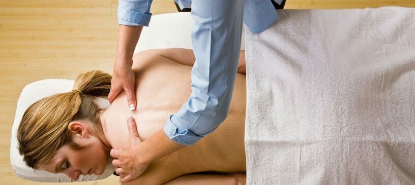 A massage professional preforms work on a client laying on a massage table. 