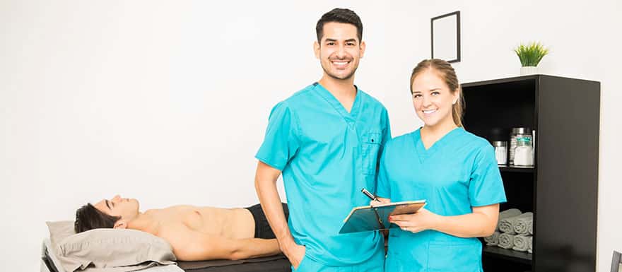 Two Massage Therapists standing in front of a client laying on a table.